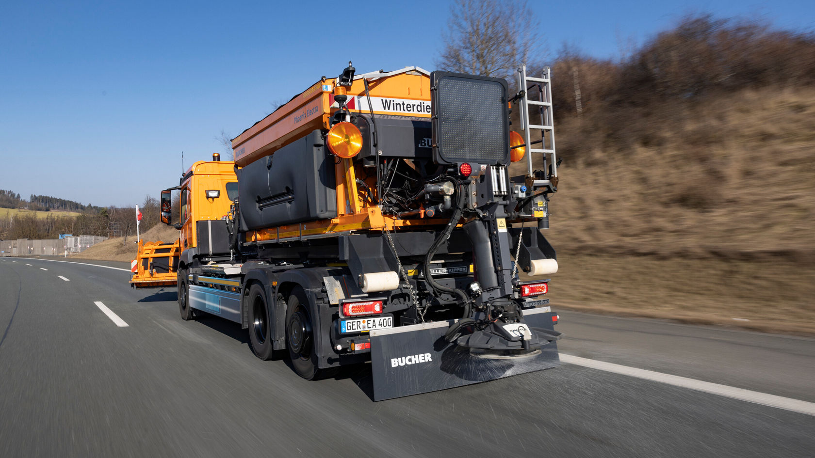 Ein Mercedes-Benz eActros fährt auf einer Straße, ausgestattet mit einem Winterdienst-Anbaugerät zur Schneeräumung.