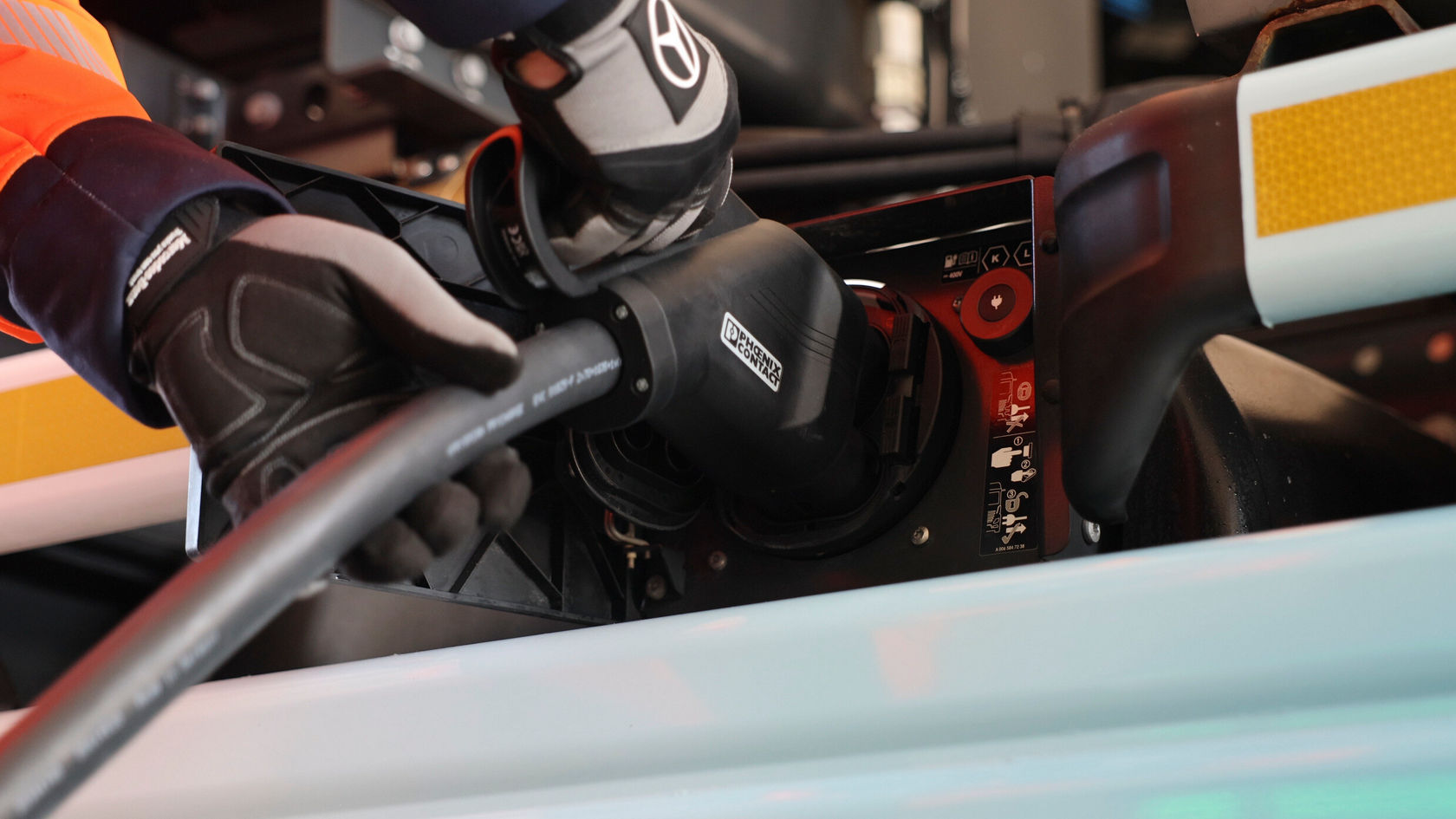 Ein Arbeiter in Handschuhen verbindet ein Ladekabel mit dem Elektrofahrzeug Mercedes-Benz eActros. Der Fokus liegt auf der Ladeschnittstelle des Fahrzeugs.