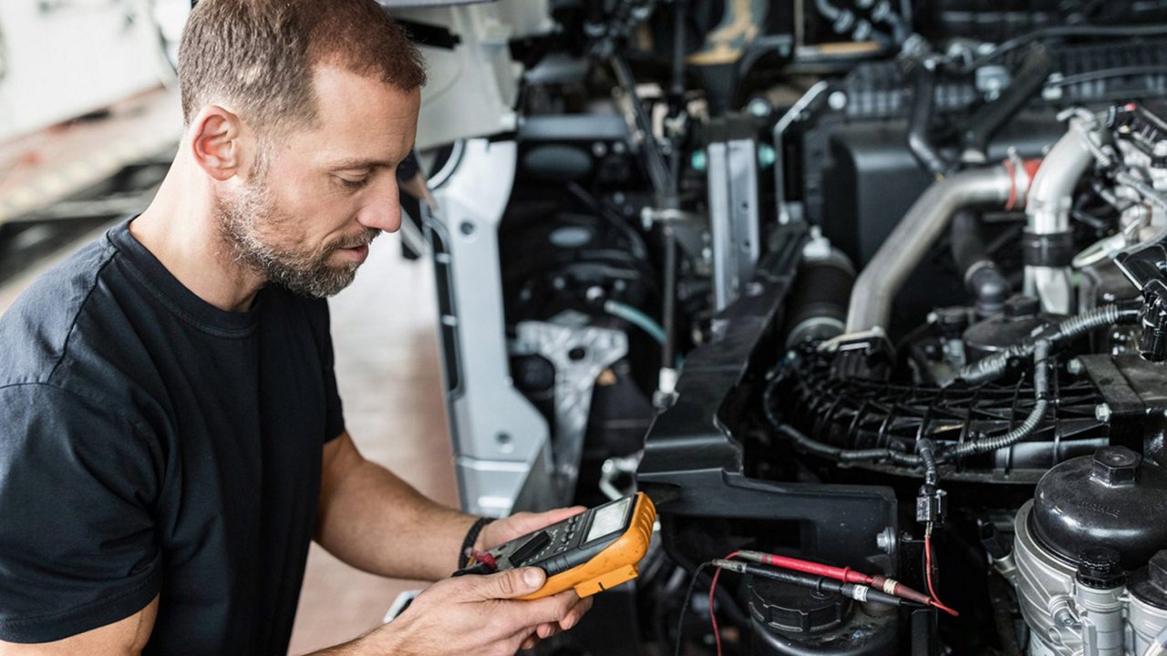 Mechaniker misst mit Multimeter im Motorraum.