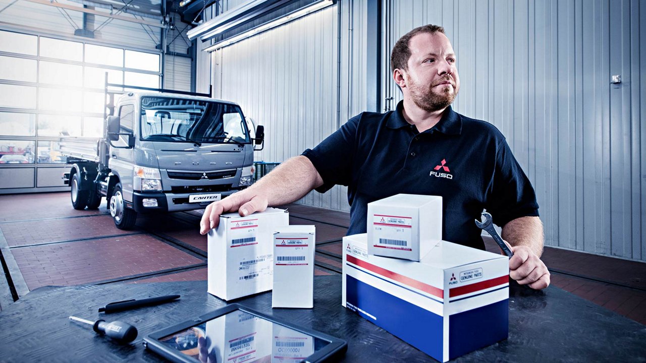 Een monteur heeft een steeksleutel in zijn hand. Zijn andere hand houdt een aantal dozen vast waarin onderdelen zitten.