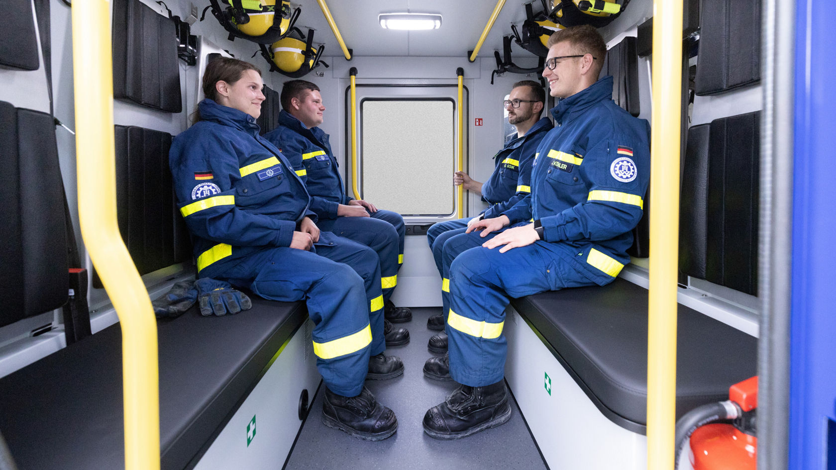 Quatre intervenants portant des vestes bleues avec des bandes réfléchissantes jaunes sont assis dans un Atego.