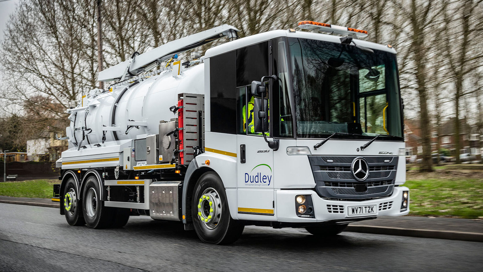Ein Mercedes-Benz Econic Müllabfuhrfahrzeug fährt auf einer Straße. Auf der Seite ist das Wort "Dudley" sichtbar, während der Fahrer das Fahrzeug steuert.