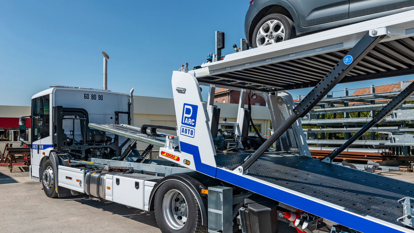 Un camión Mercedes-Benz Econic con una plataforma elevadora preparada para cargar o descargar vehículos está estacionado en un aparcamiento.