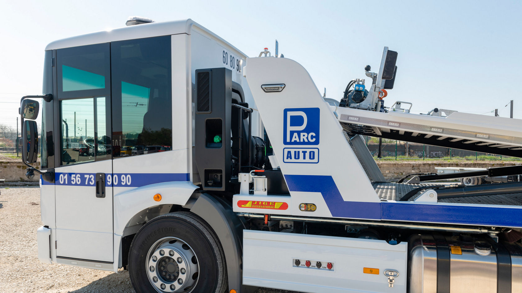 Un camión Mercedes-Benz Econic con una plataforma elevadora, vista lateral, sobre suelo sin pavimentar. El vehículo está diseñado para el transporte de automóviles.