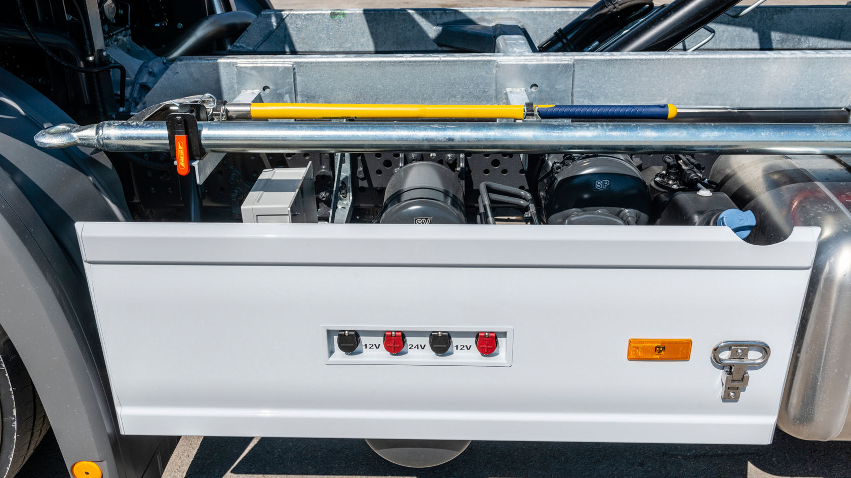 La unidad de almacenamiento lateral de un Mercedes-Benz Econic con interruptores visibles para conexiones eléctricas, una herramienta y una llave, que se utilizan para fines de mantenimiento.
