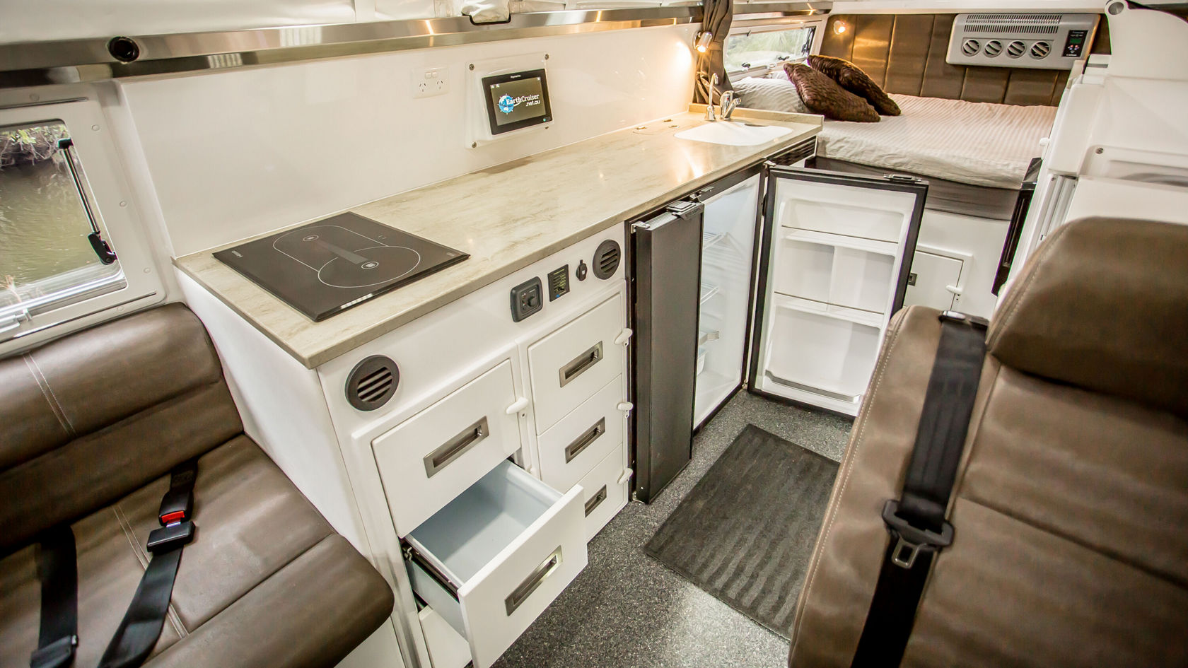 Ein kompakter Küchenbereich in einem Wohnmobil mit einer Arbeitsplatte, einem Kochfeld, einem Kühlschrank und Schubladen.