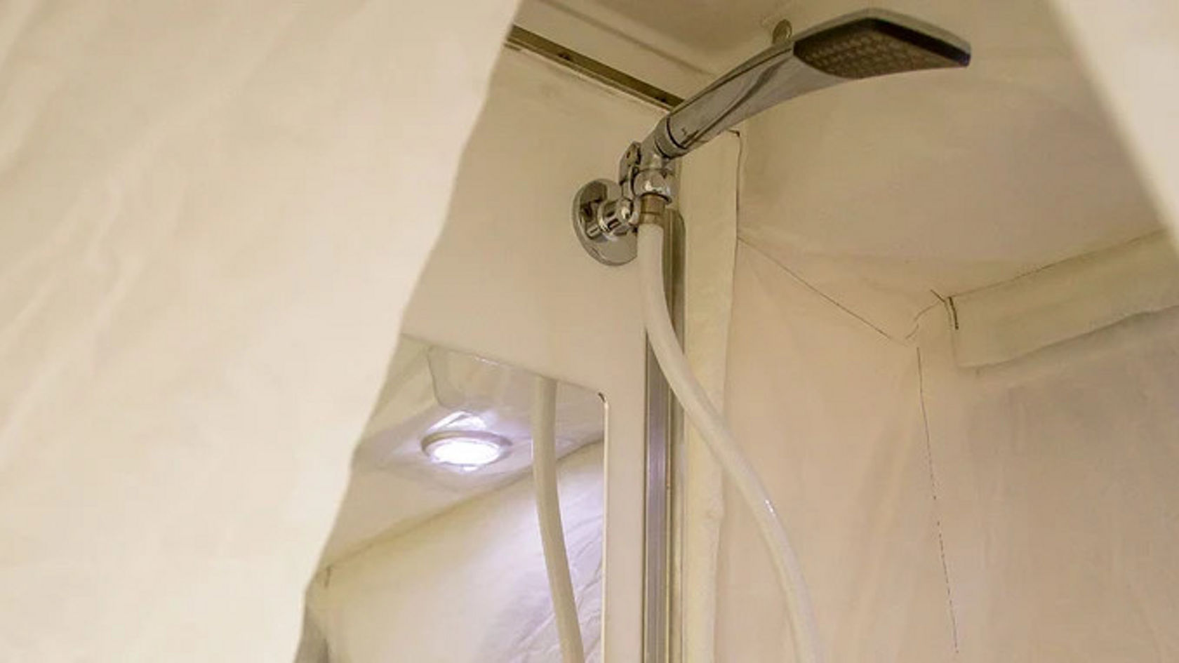 Eine Dusche in einem kleinen, hellen Raum mit einem Duschkopf an der Wand.