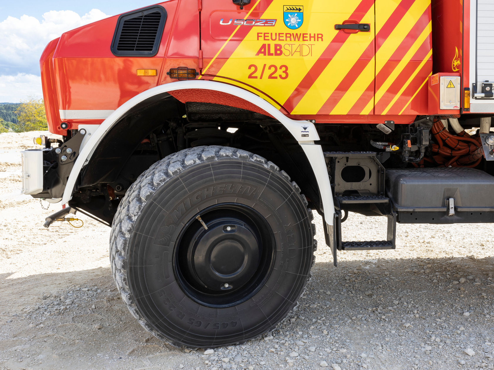 Seitenansicht eines Feuerwehrfahrzeugs in Rot mit gelben Streifen und der Aufschrift "Feuerwehr Albstadt". Deutlich sichtbar ist das große Rad und die Gerätschaften am Fahrzeug.