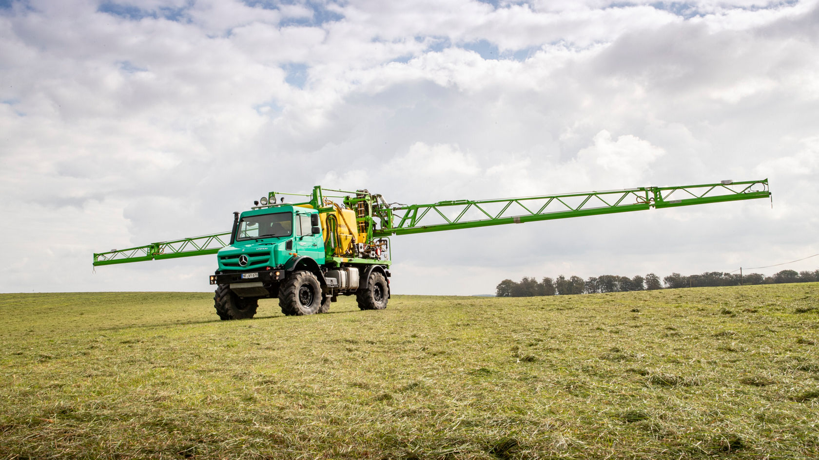 Ein Mercedes-Benz Landmaschinenfahrzeug mit einem langen Spritzarm steht auf einem Feld. Die grüne Maschine ist für landwirtschaftliche Anwendungen ausgelegt.