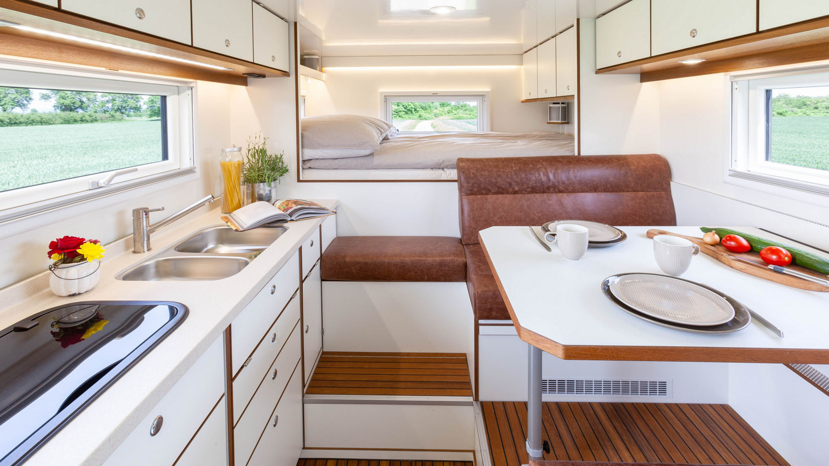 Interior of a motorhome with a fully equipped kitchen and a sleeping area in the background.