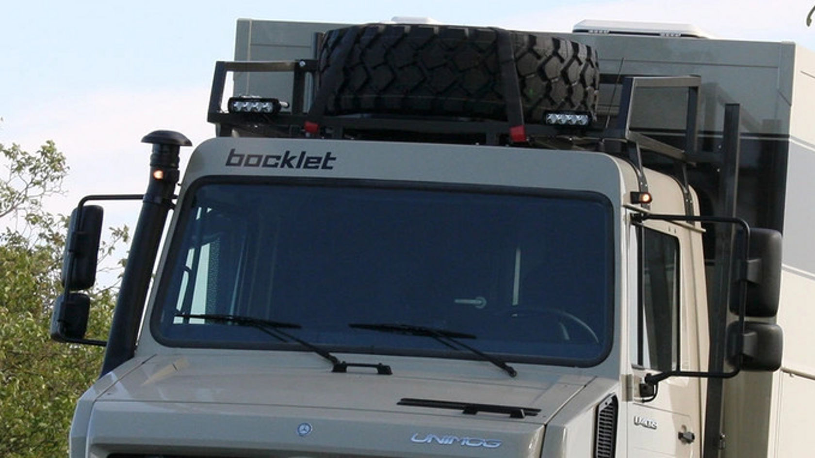 A Mercedes-Benz Unimog with a spare tire on the roof rack.