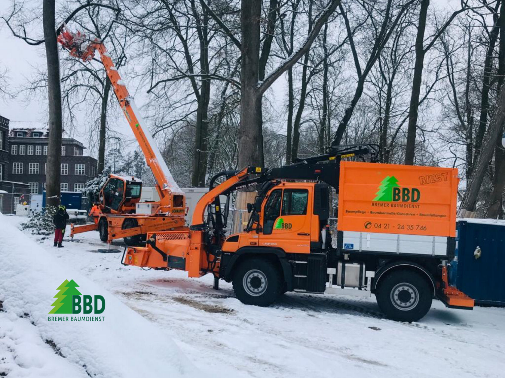 Un véhicule orange de Bremer Baumschnittdienst, équipé d'un broyeur de bois, est garé dans la neige. Le véhicule porte le logo et les coordonnées de l'entreprise sur le côté.