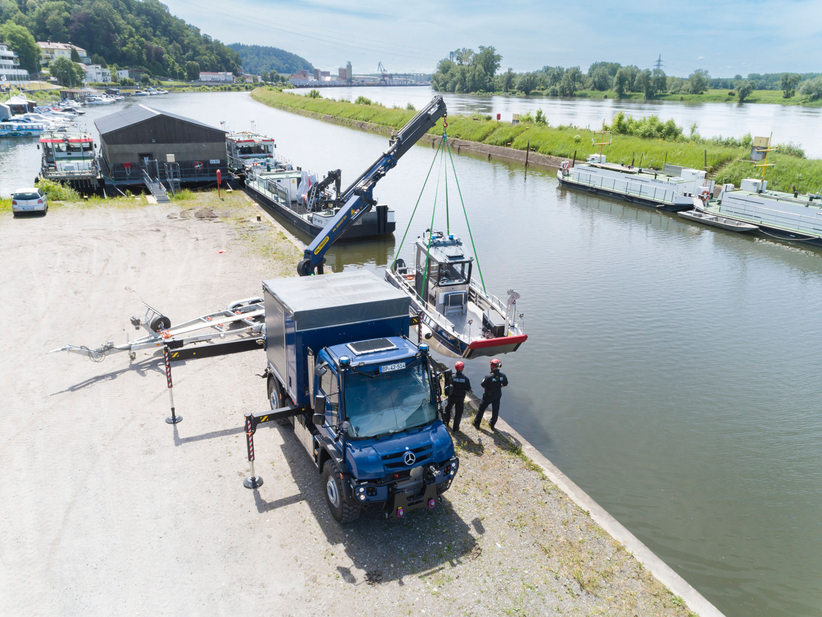 Ein Mercedes-Benz Unimog hebt mit einem Kran ein Boot am Wasser.