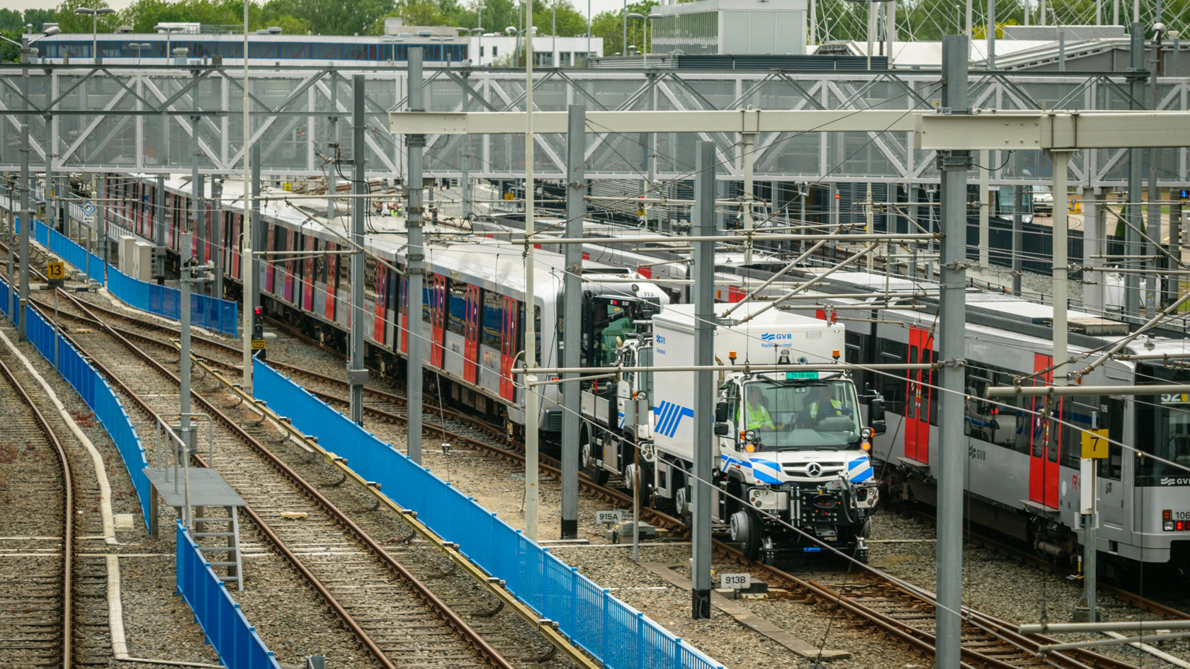 Ein Mercedes-Benz Unimog steht auf den Gleisen einer Rangierbahnhofanlage, umgeben von mehreren Zügen. Die Szene zeigt die typischen Gleisanlagen und Betriebsgebäude.
