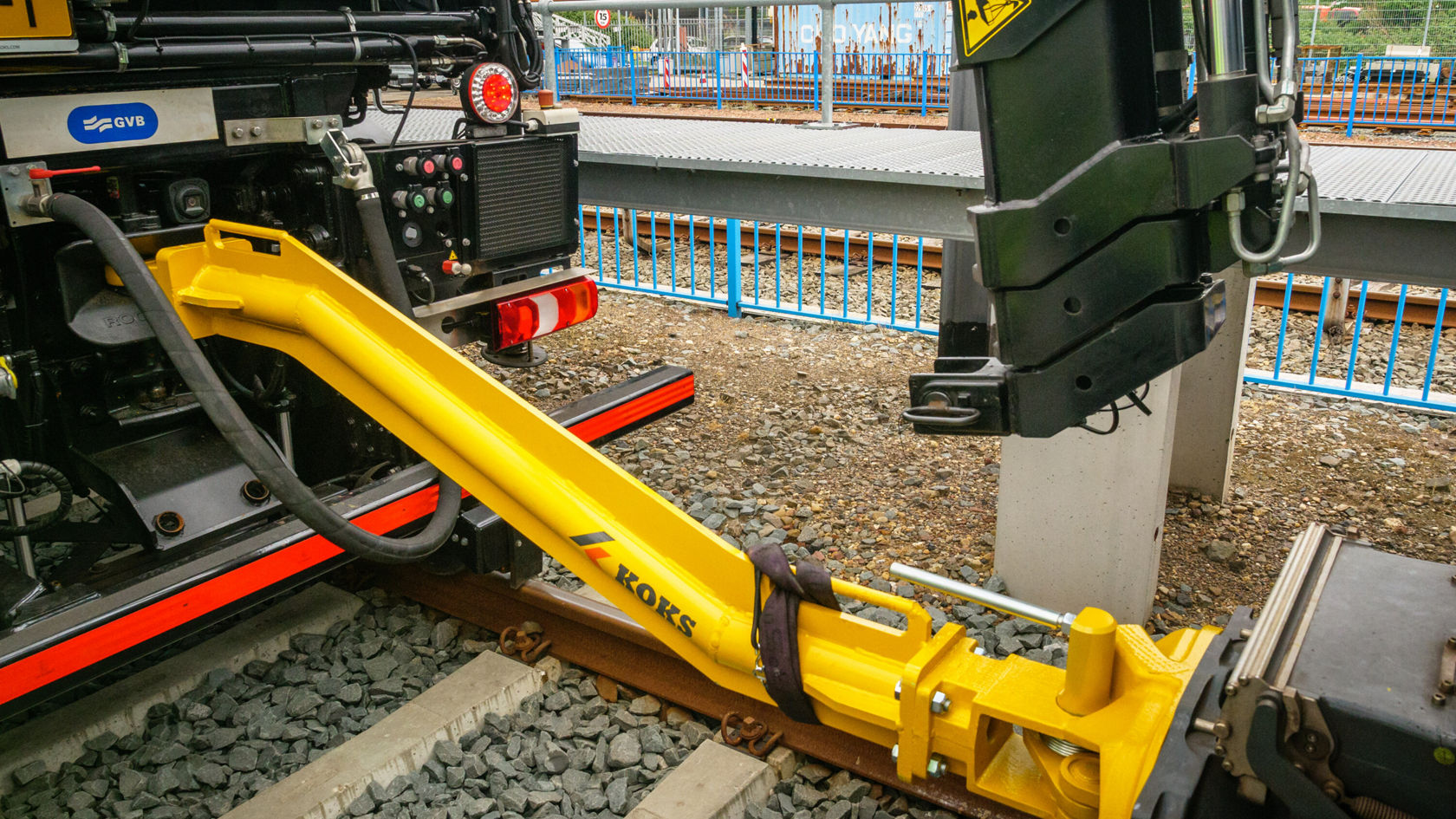 Ein gelbes Anbaugerät einer Maschine, das auf einem Schienenstück montiert ist. Das Gerät gehört zur Kategorie Gleisbau und wird für Wartungsarbeiten eingesetzt.