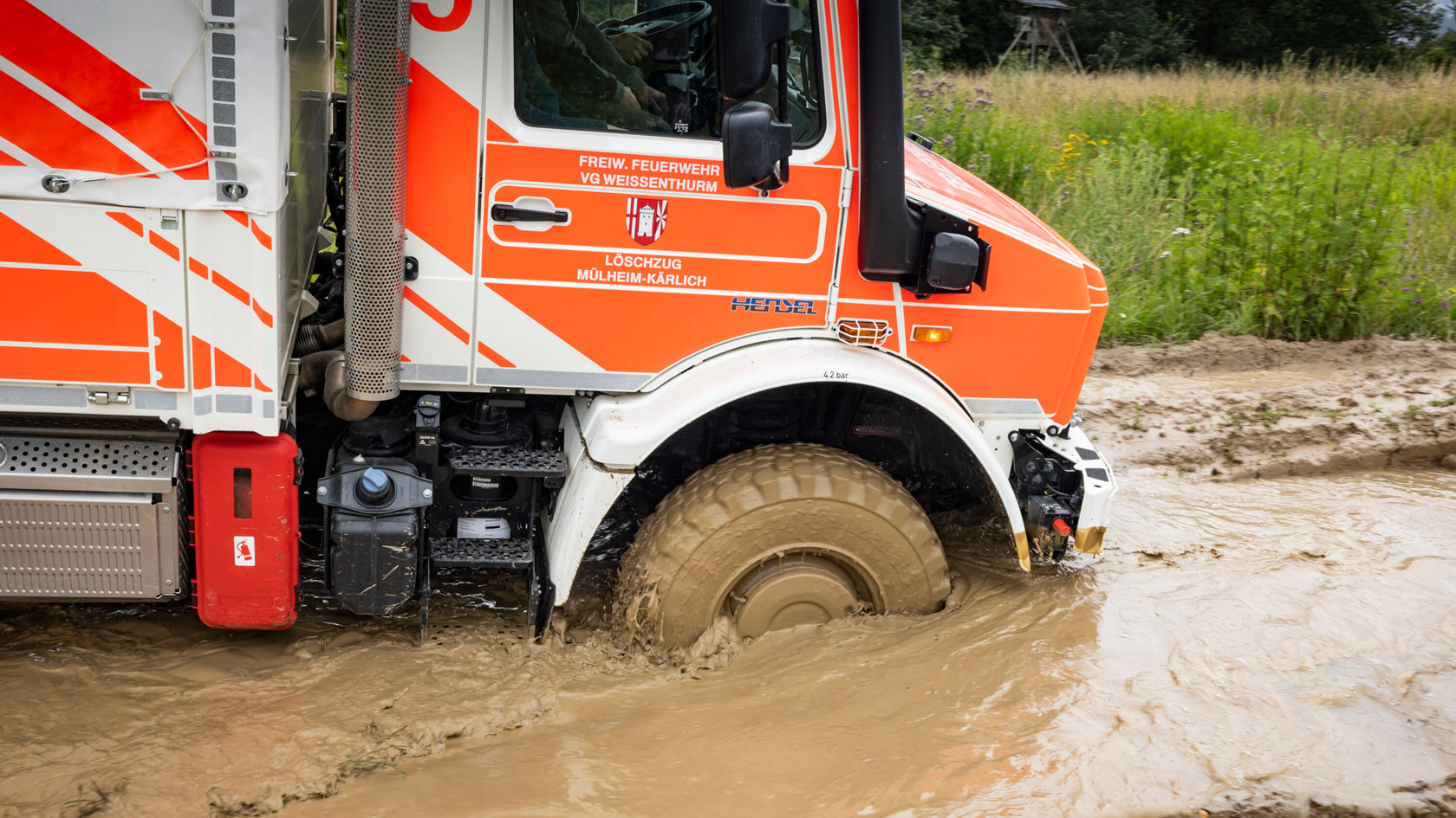 Un Unimog Mercedes-Benz traverse des eaux boueuses.