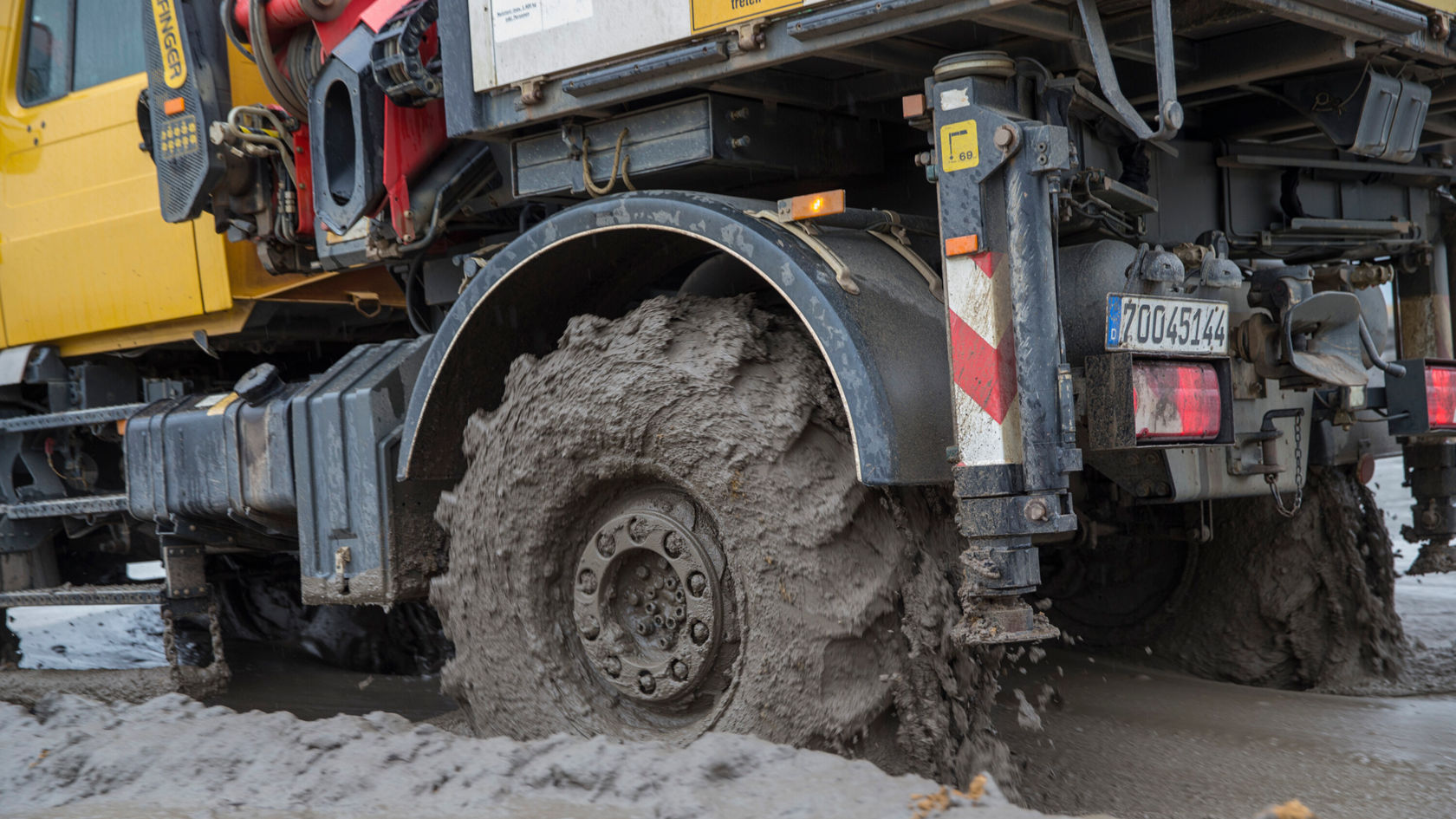 An off-road vehicle with the Mercedes-Benz logo drives through muddy terrain, its tyres deep in the mud and throwing up dirt.