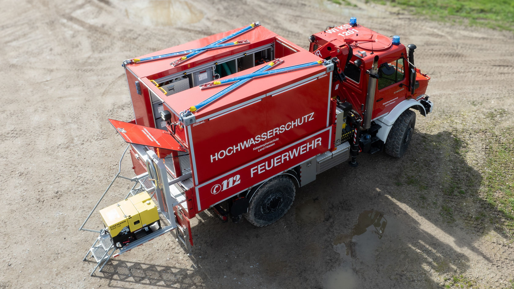 Un véhicule d'incendie rouge destiné à la protection contre les inondations, avec des conteneurs ouverts montrant les équipements et matériels pour l'intervention. La surface du véhicule est bien visible.