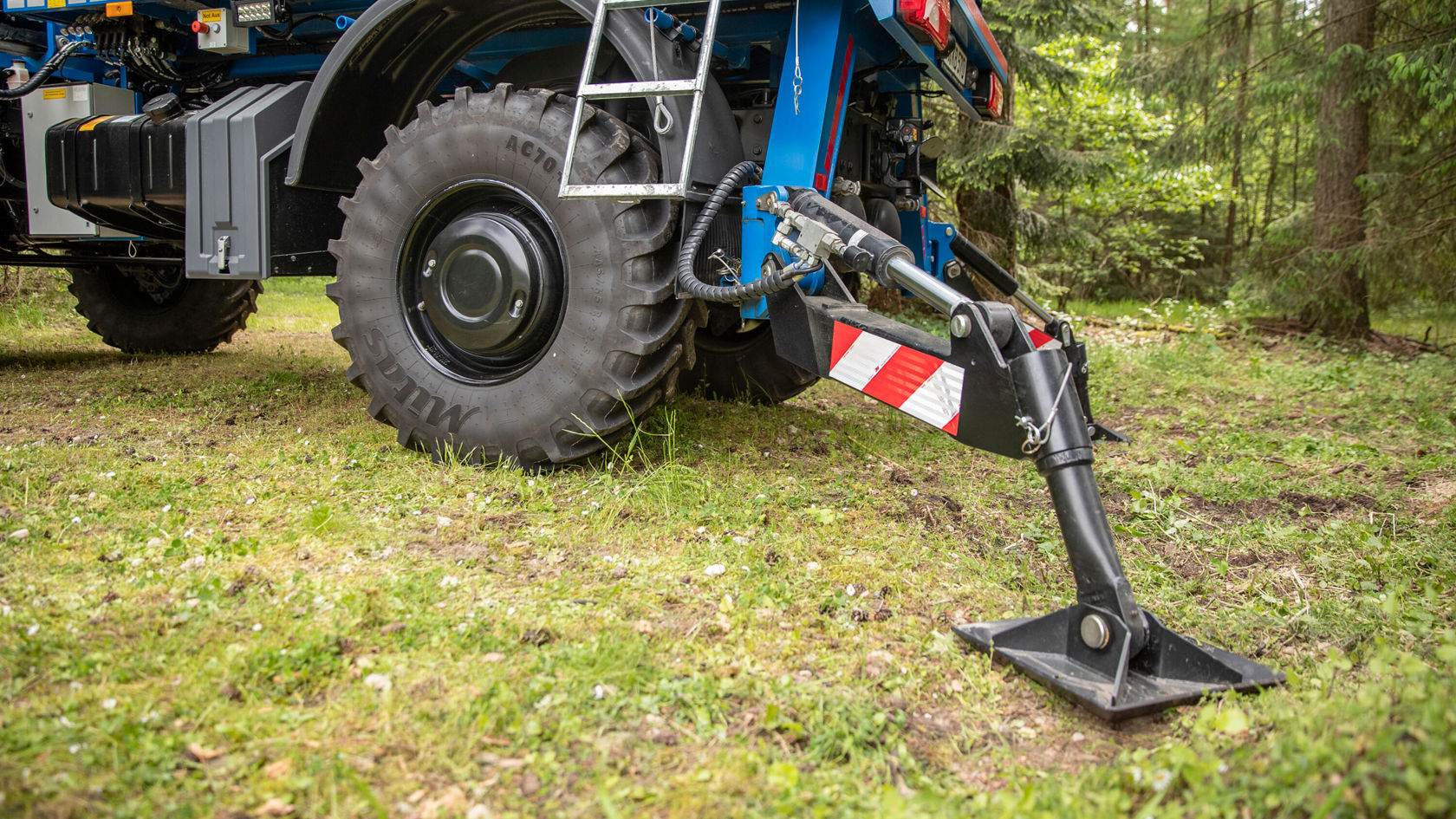 Un tractor Mercedes-Benz está en una pradera, con un implemento en funcionamiento que se utiliza para la preparación del suelo. Los neumáticos son grandes y robustos, adecuados para terrenos sin pavimentar.