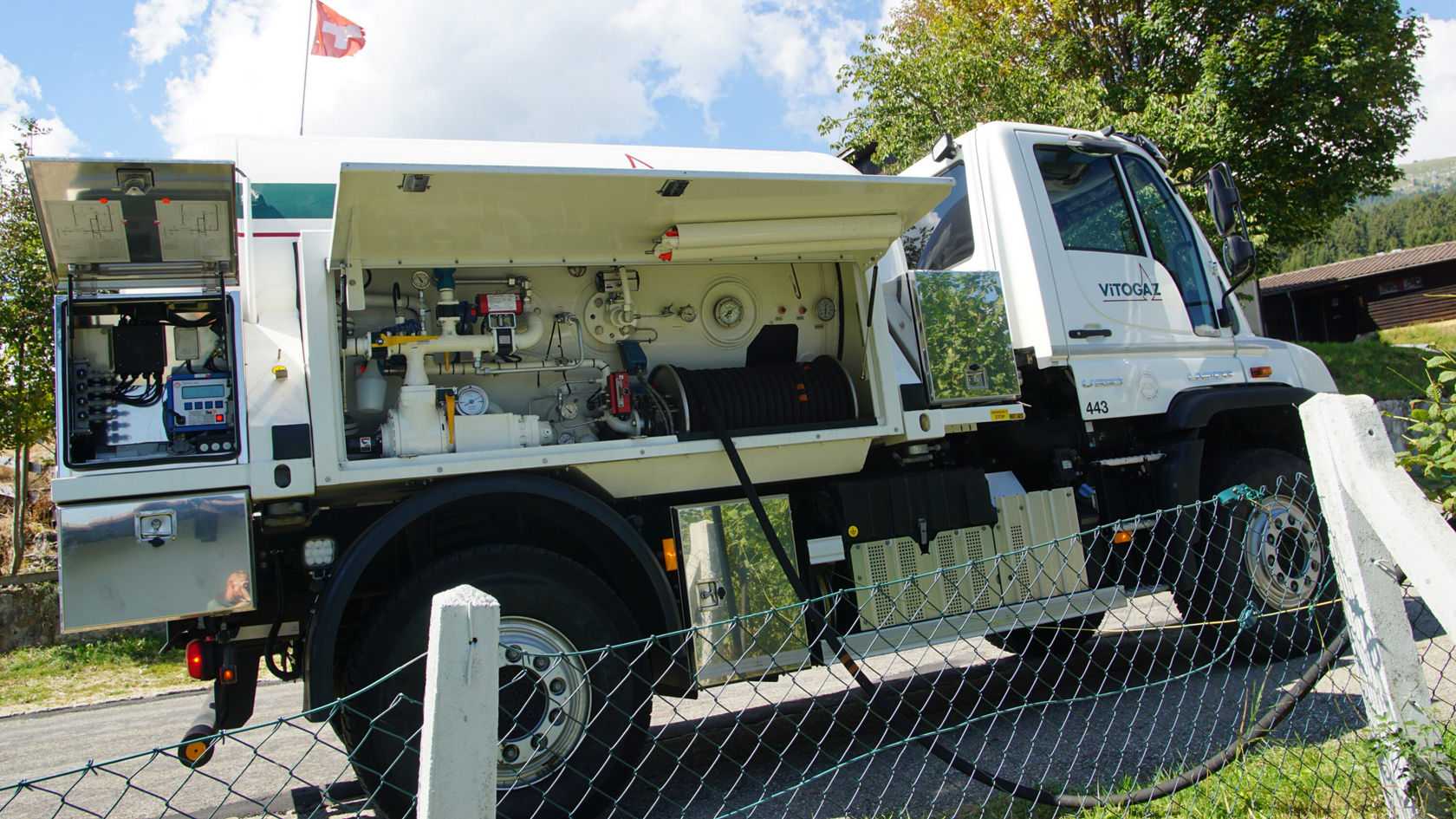 Ein Mercedes-Benz Unimog mit offenem Aufbau, der verschiedene Werkzeuge und Ausrüstungen für technische Einsätze zeigt, steht an einer Straße umgeben von Bäumen.