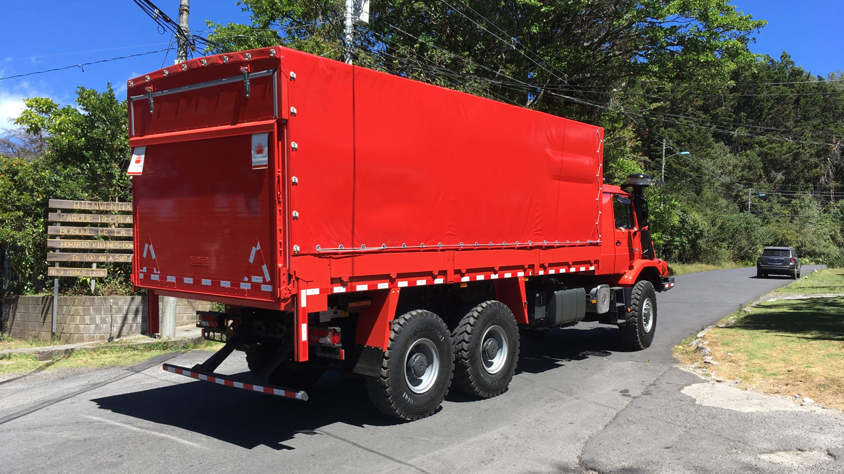 Un camion rouge avec un grand espace de chargement est stationné sur une route. L'arrière du véhicule présente des bandes réfléchissantes et une plate-forme de chargement ouverte.