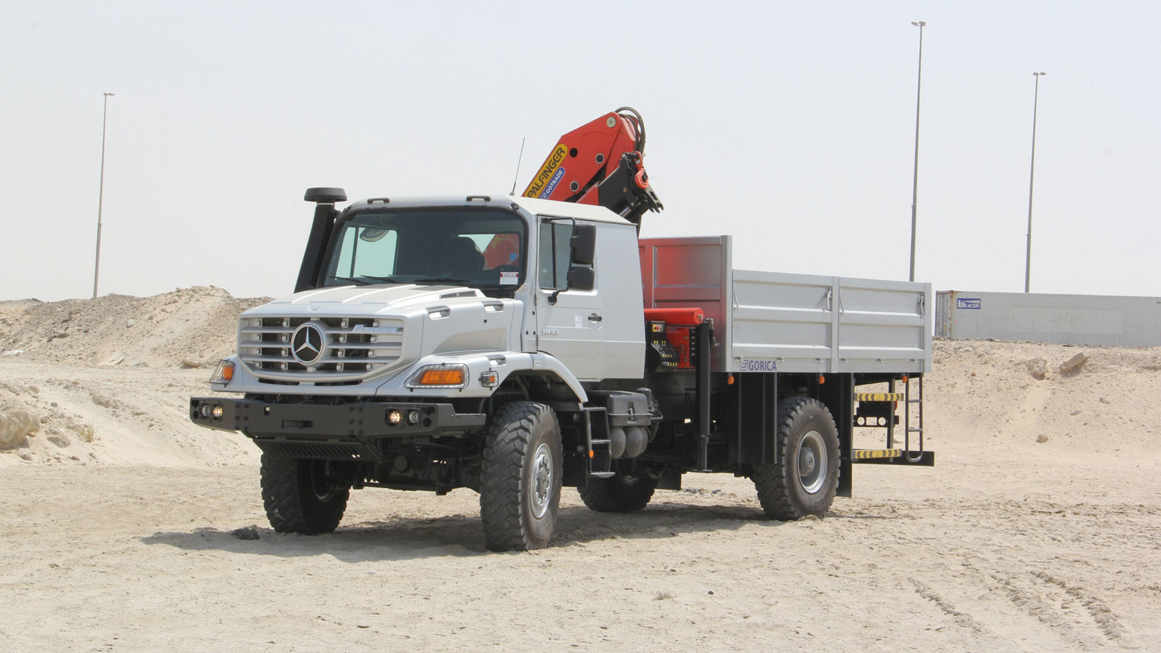 Robust Mercedes-Benz Zetros truck with a crane attachment, positioned on a construction site. The truck has an open cargo bed and is designed for off-road work.