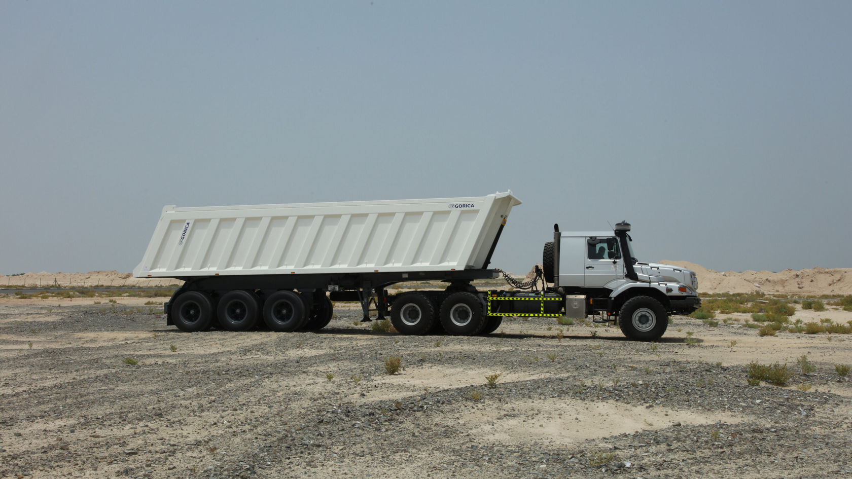 A Mercedes-Benz Zetros tipper truck stands on a gravel surface. The tipper is white with a high-sided load bed and is ready to transport material.