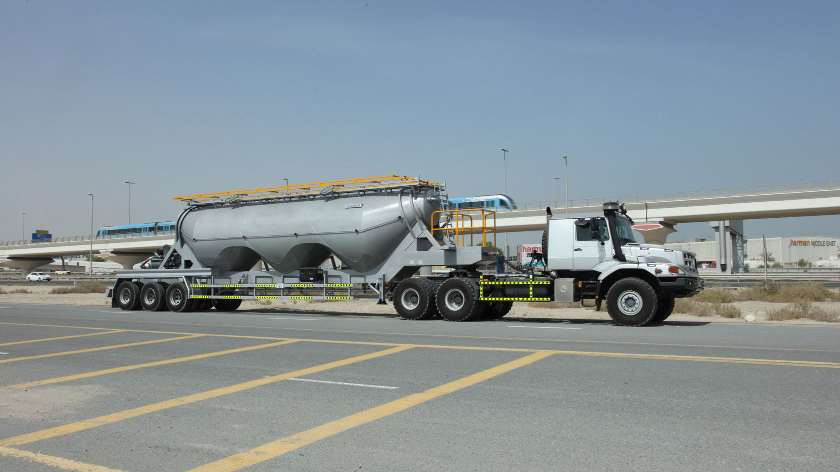 A Mercedes-Benz Zetros with a large silver container on a trailer is standing on a road in an urban environment.