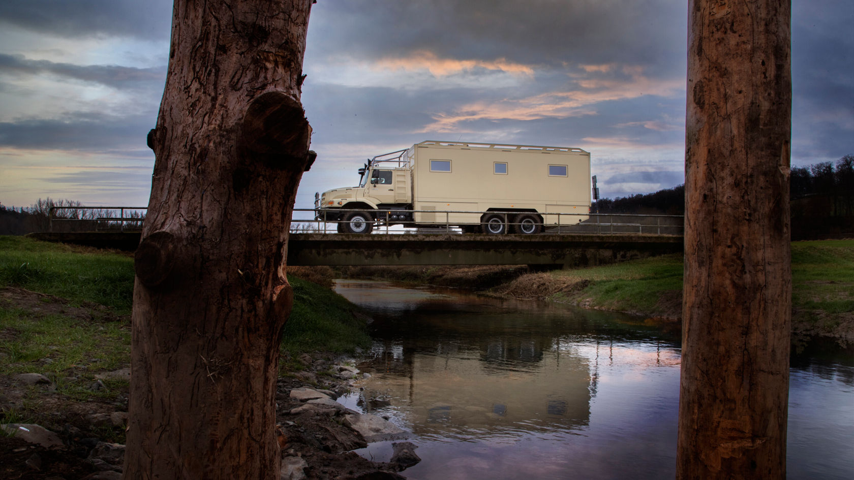 Ein Zetros Wohnmobil steht auf einer Brücke über einem kleinen Gewässer. Das Wasser reflektiert das Fahrzeug.