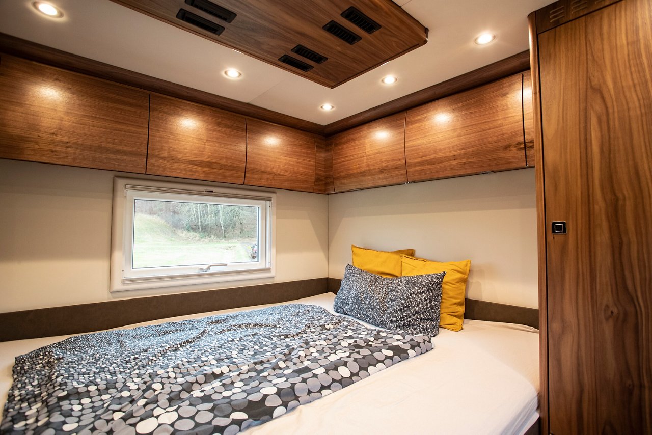 Ein Schlafzimmer mit einem Doppelbett. Holzverkleidung an den Wänden und Decke. Ein Fenster lässt Licht herein und bietet Blick nach draußen.