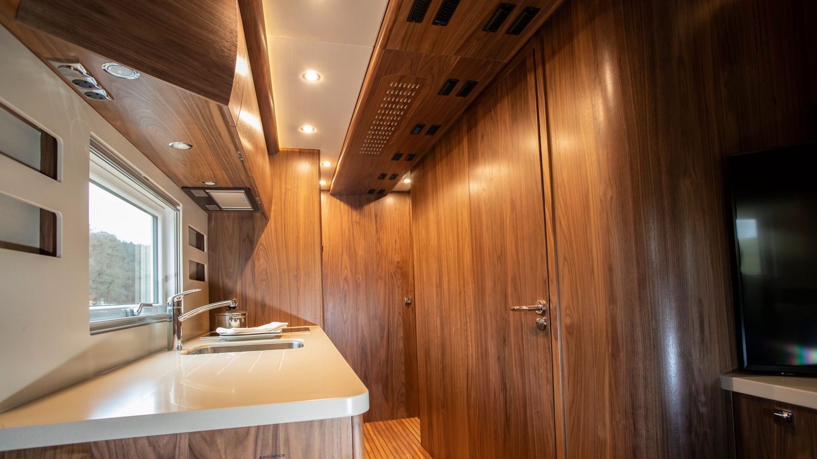 Innenraum des Zetros Wohnmobil mit Holzverkleidungund Küchenecke. Die Wand hat Fenster und Beleuchtung.