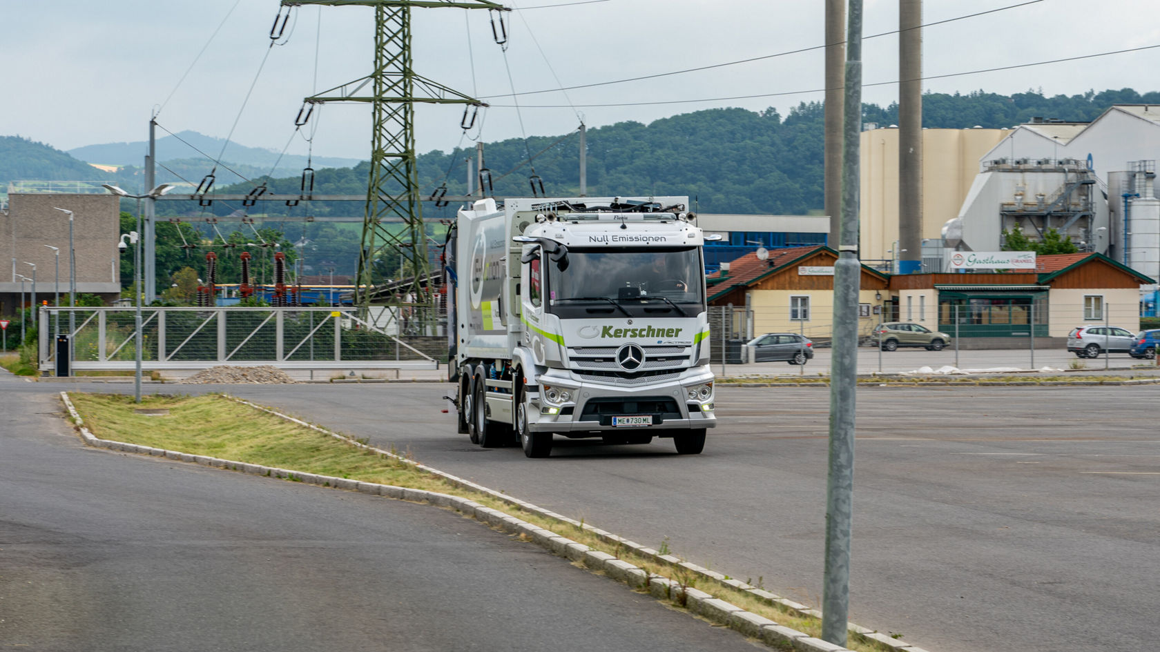 Ein Mercedes-Benz eActros fährt auf einem Unternehmensgelände, umgeben von modernen Gebäuden und Strommasten. Der Lastwagen ist mit der Aufschrift "Kerschner" versehen und zeigt eine umweltfreundliche Lieferoption.