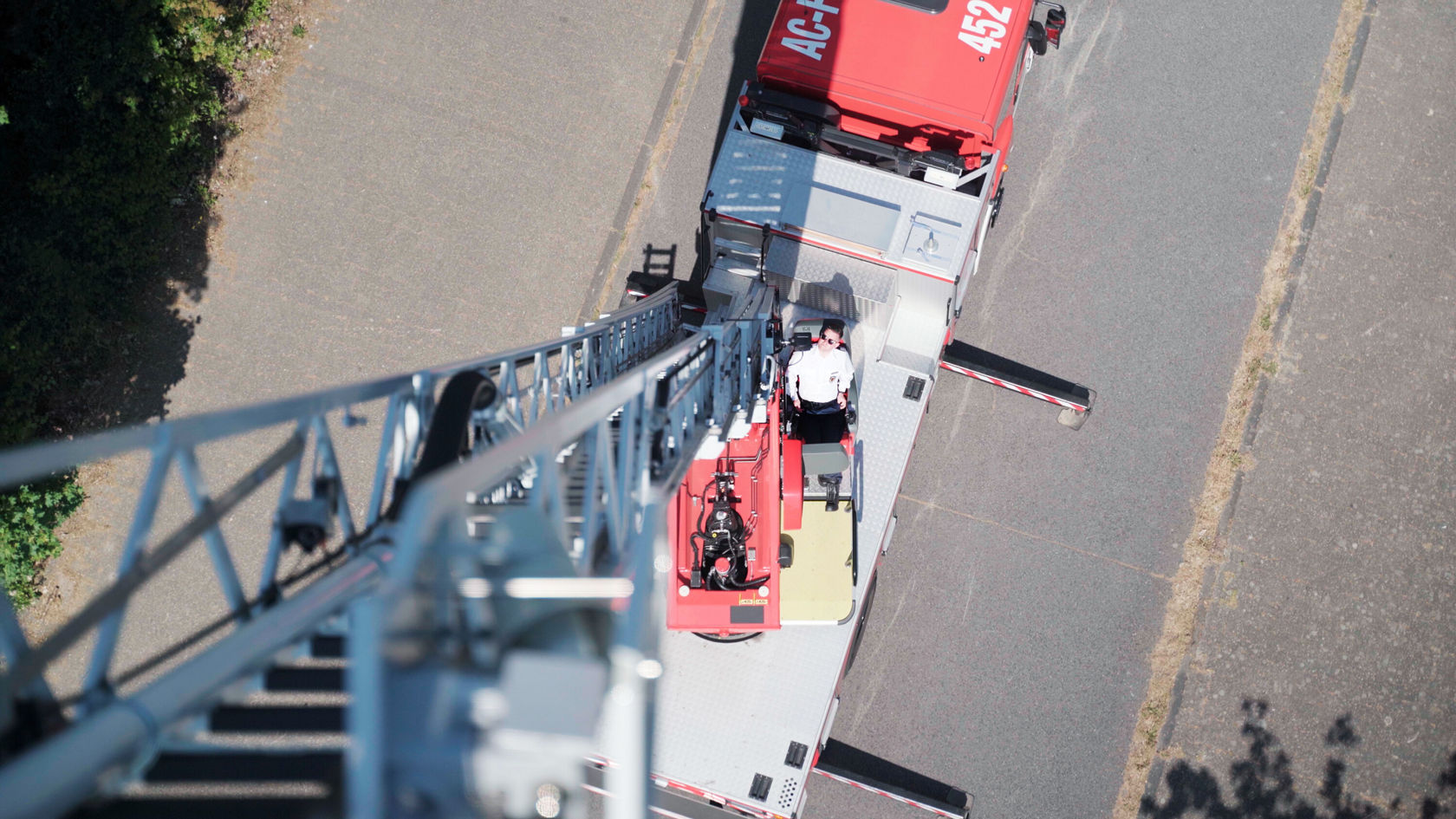 A fire ladder viewed from above, with a firefighter sitting on the vehicle that is parked on a street.