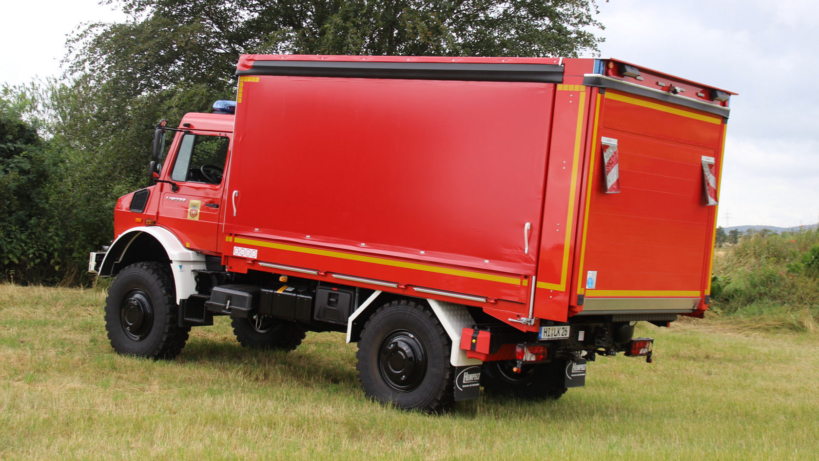 Ein roter Mercedes-Benz Lkw steht in einer Wiese, mit einem großen geschlossenen Laderaum, der für Transportzwecke genutzt wird.
