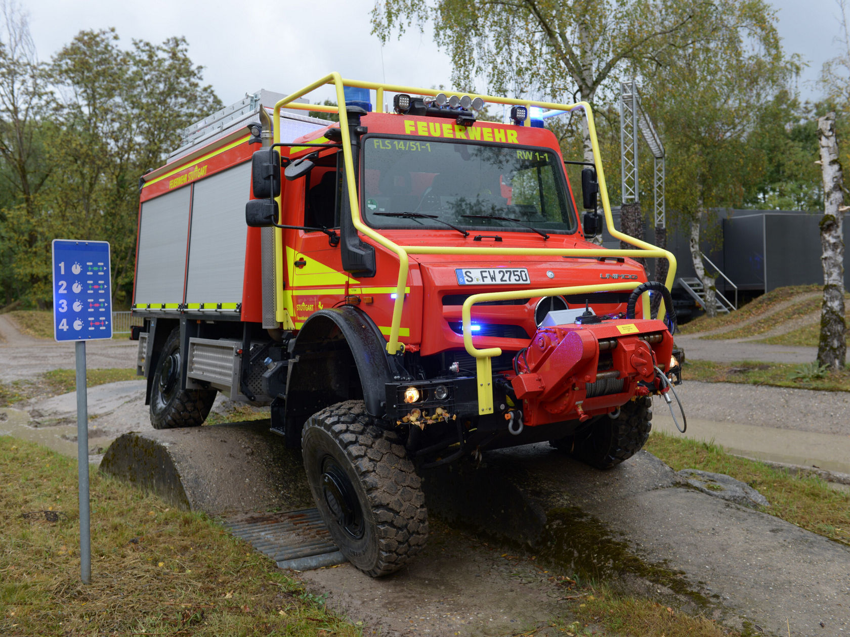 Ein rotes Feuerwehrfahrzeug der Marke Mercedes-Benz steht auf einem unebenen Gelände. Es ist mit einem auffälligen Rettungs- und Löschsystem ausgestattet.