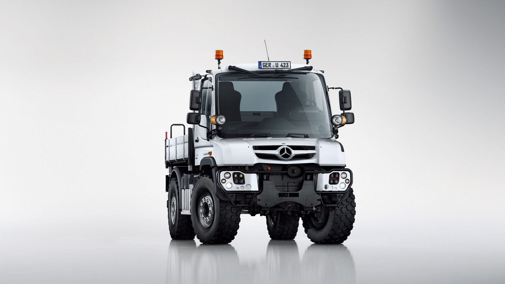 Un Unimog Mercedes‑Benz de couleur blanche est vu de face sur un fond neutre.