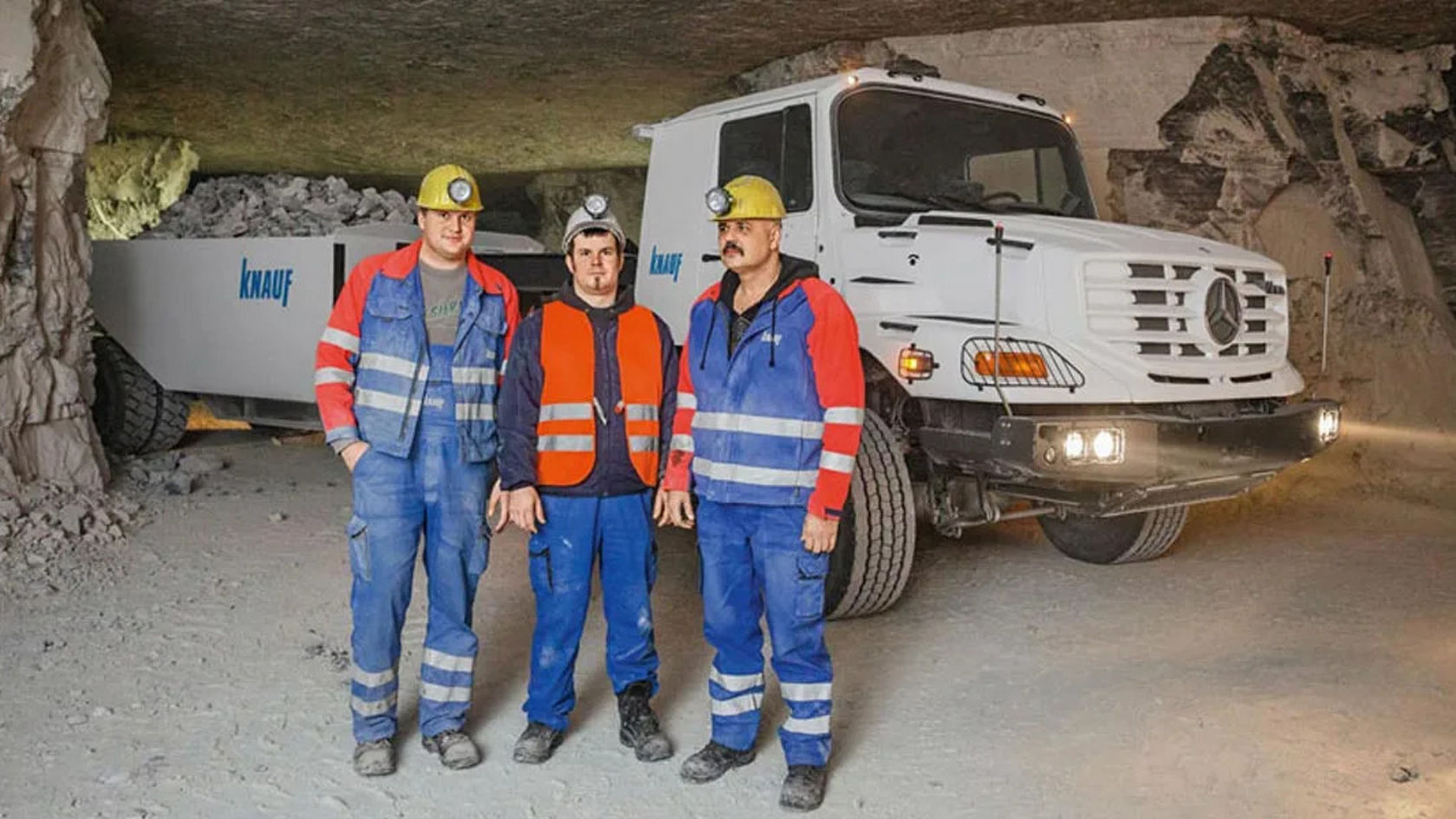 Trois mineurs se tiennent sous terre devant un Zetros Mercedes‑Benz.