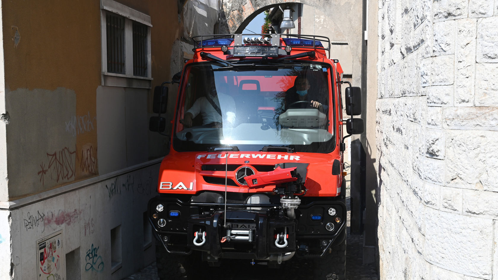 Ein rotes Mercedes-Benz Unimog Feuerwehrfahrzeug fährt durch eine enge Gasse..