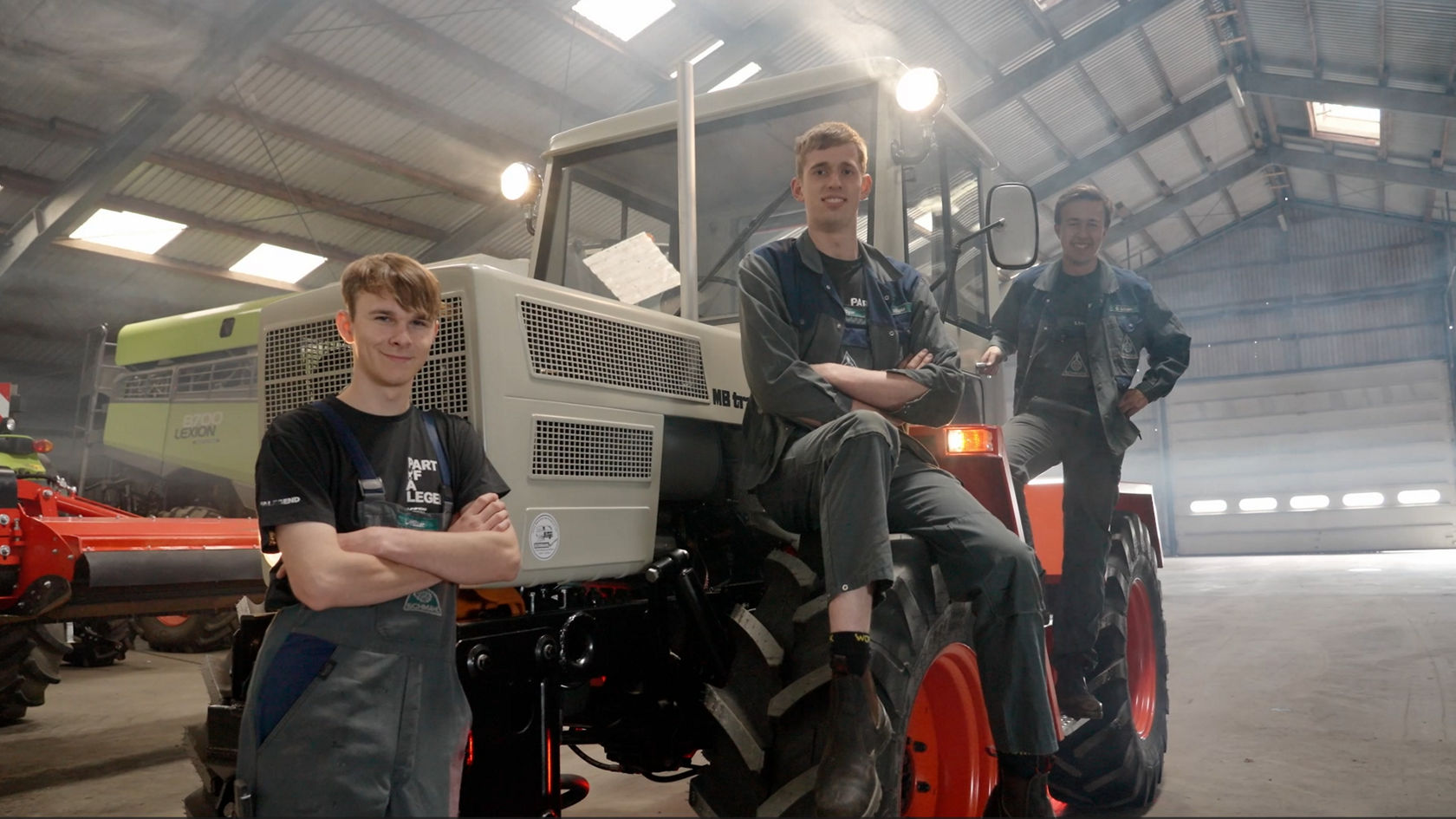Drie jonge mannen staan voor een Mercedes-Benz tractor. Ze dragen werkkledij en glimlachen naar de camera.