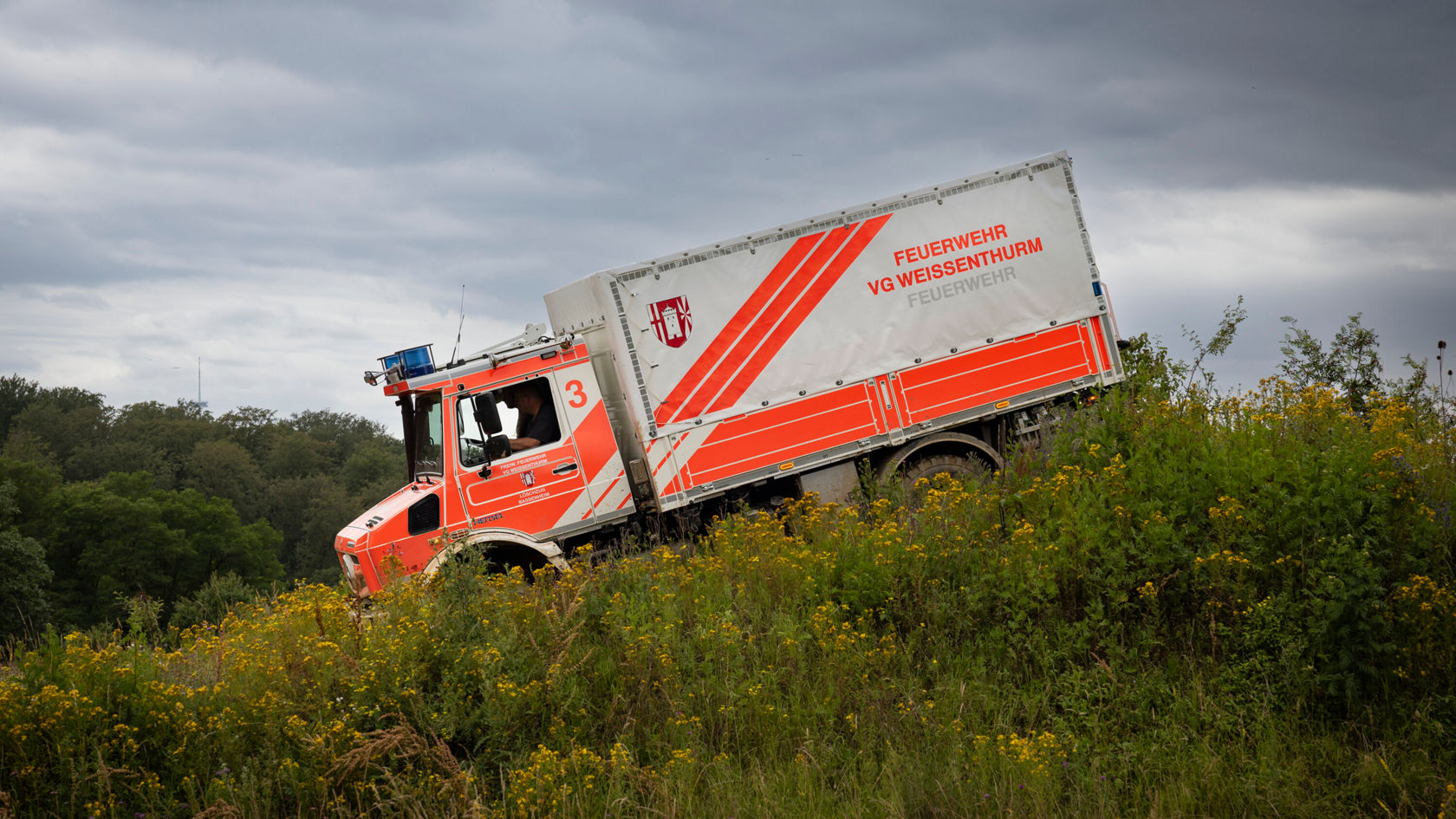 Ein Mercedes-Benz Unimog, ausgestattet für den Rettungsdienst, fährt einen Hügel hinab.