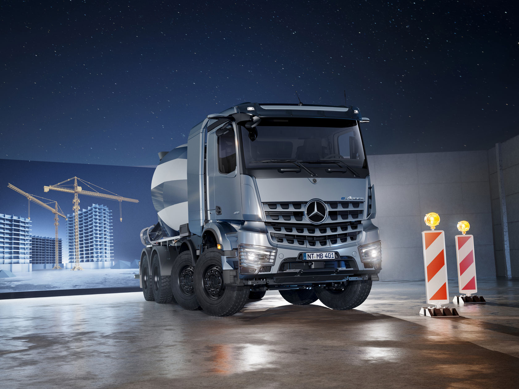De afbeelding toont een blauwgrijze Mercedes-Benz eArocs betonmixer die in een hal staat. Op de achtergrond is op een led-wand een gesimuleerde scène te zien van een bouwproject bij nacht met verlichte kranen en ruwbouw onder een sterrenhemel. Voor de vrachtwagen staan twee rood-wit gestreepte waarschuwingsbakens met gele zwaailichten.