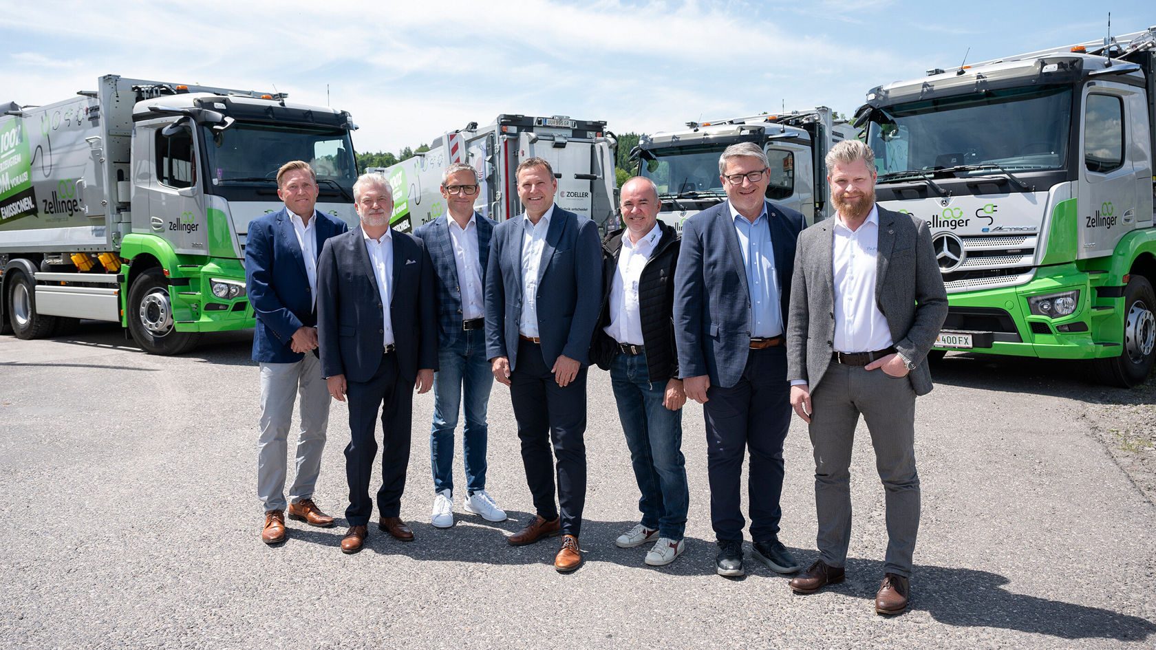 Eine Gruppe von sieben Personen steht in einem Freigelände vor mehreren Mercedes-Benz eActros Nutzfahrzeugen.