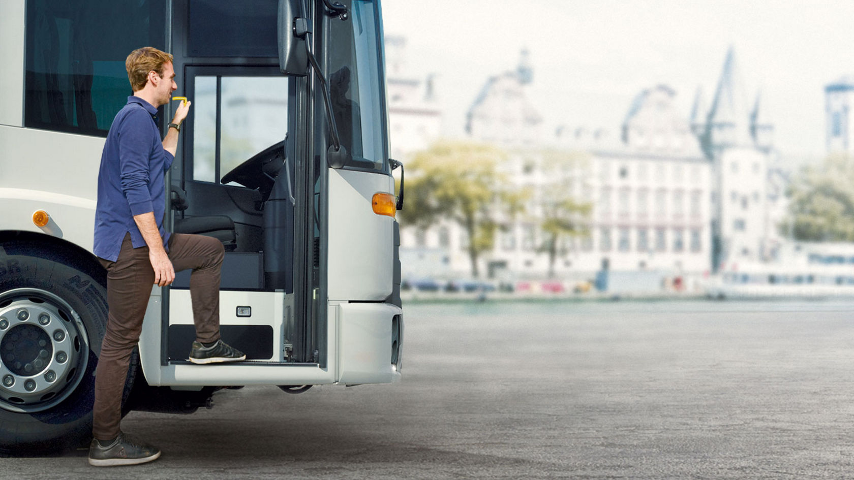 Un homme en chemise bleue et pantalon marron monte dans un Econic côté passager. Le camion se trouve sur une place asphaltée, un décor urbain est visible dans un arrière-plan flou.