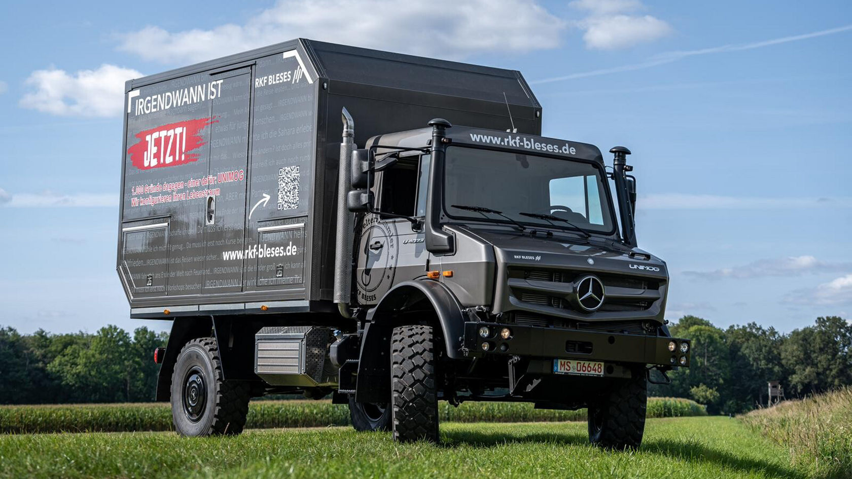 An all-terrain Unimog stands on a meadow under a blue sky.