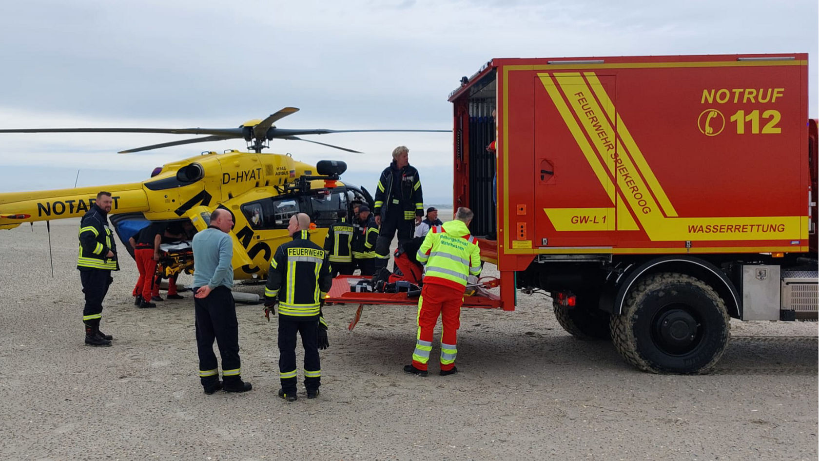Unimog mit geöffneter Heckklappe, dahinter ein Rettungshubschrauber, drumherum stehen Einsatzkräfte