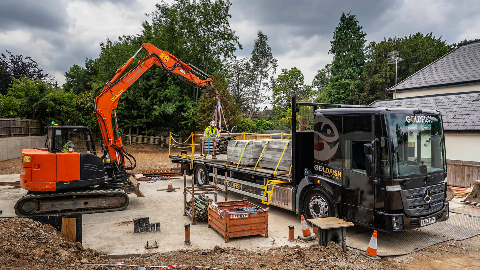 Ein Mercedes-Benz Econic steht auf einer Baustelle neben einem Bagger, der Material von einem Anhänger ablädt.