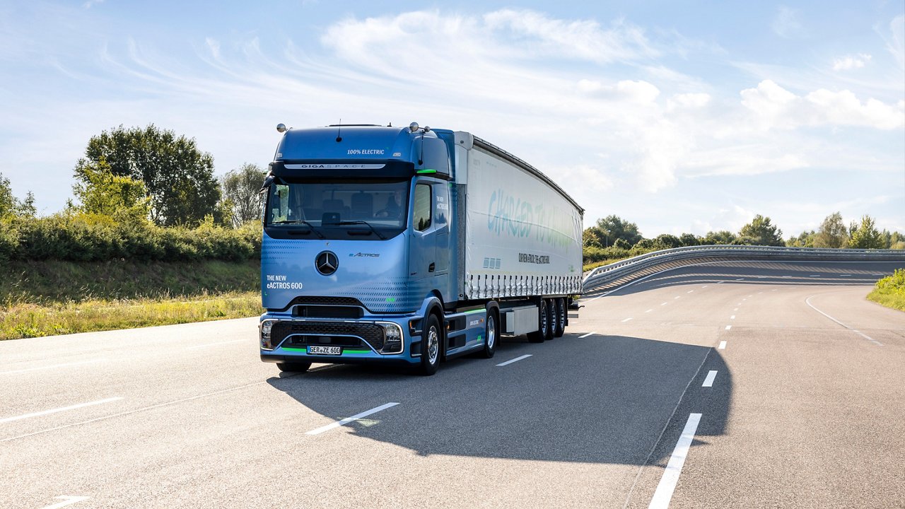 Blauer Elektro-Lkw mit Sattelauflieger auf einer leeren Autobahn bei Sonnenschein.