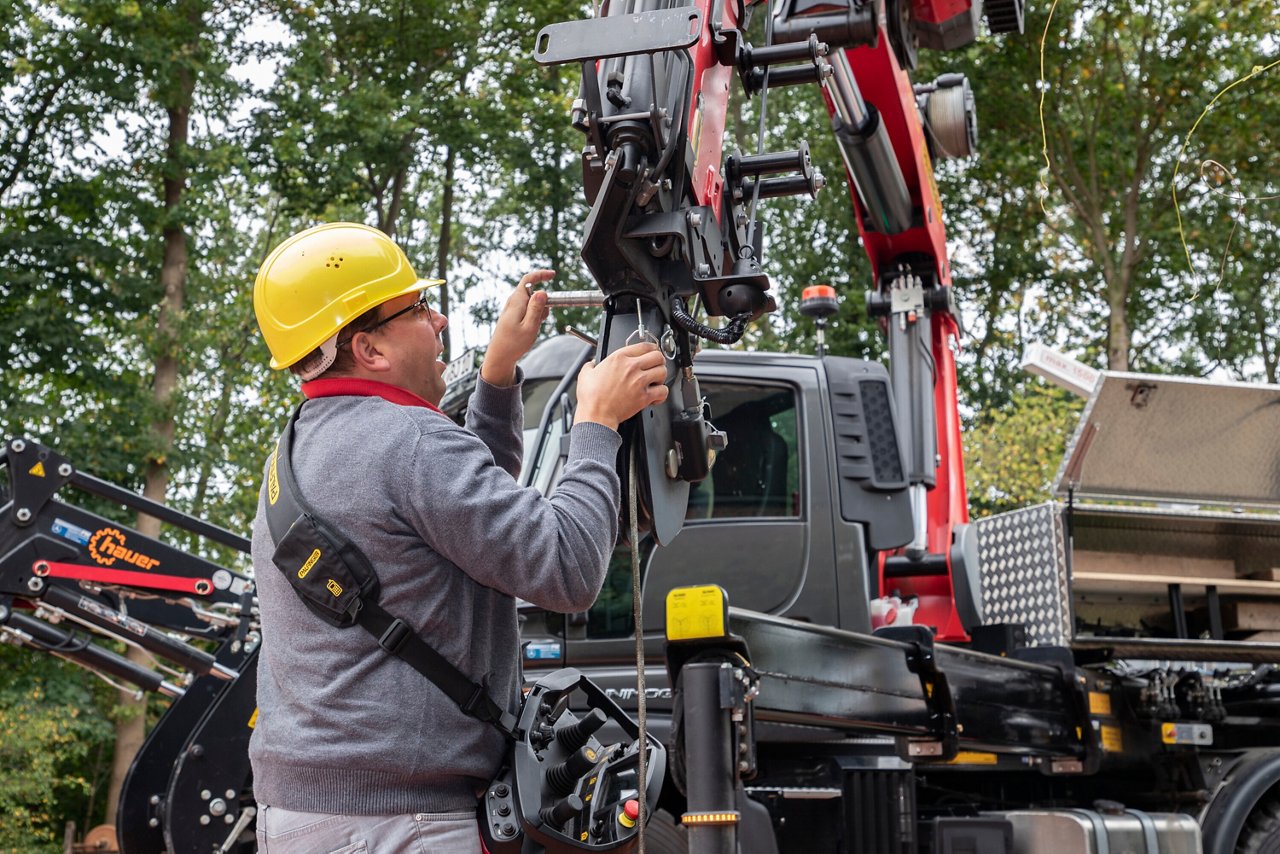 A worker with a yellow helmet and a gray work jacket is mounting a part on a crane.