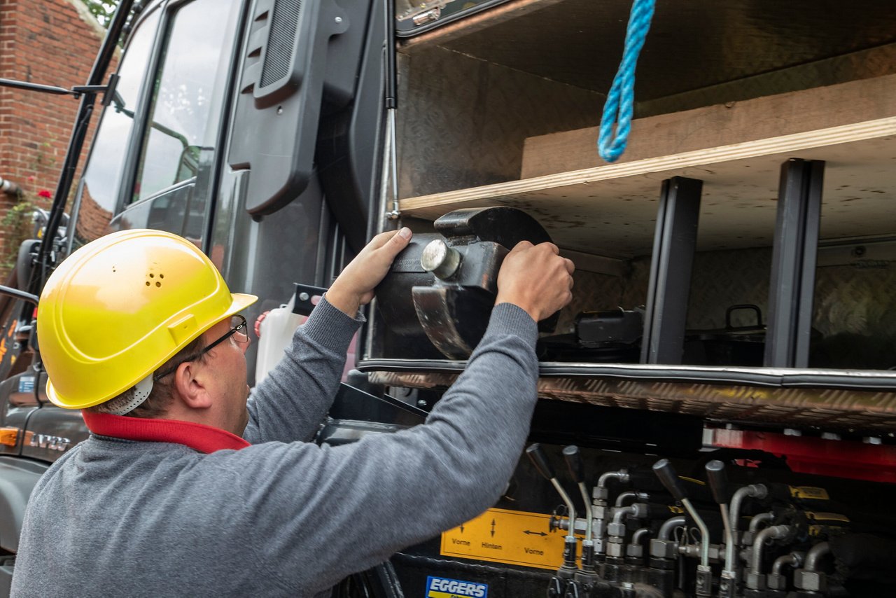A person wearing a yellow helmet is working on the side wall of a vehicle.