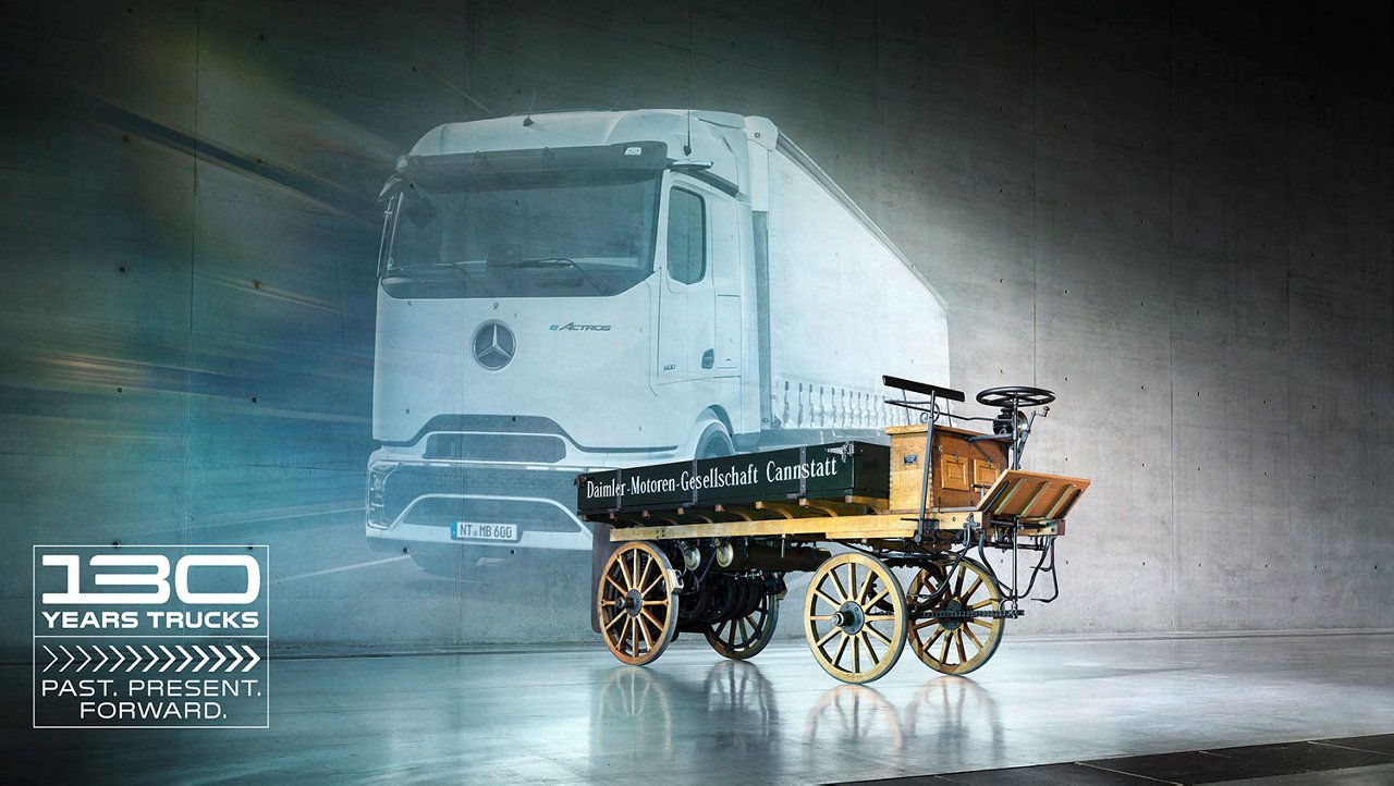 Storico camion con motore Daimler davanti a un moderno eActros bianco in un padiglione espositivo.